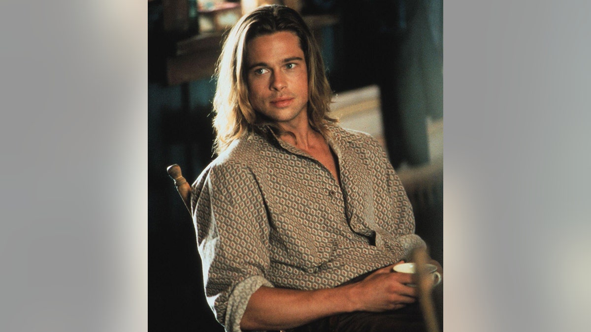 Brad Pitt in a button down shirt with shoulder lenght hair as Tristan in "Legends of the Fall" sitting in a chair