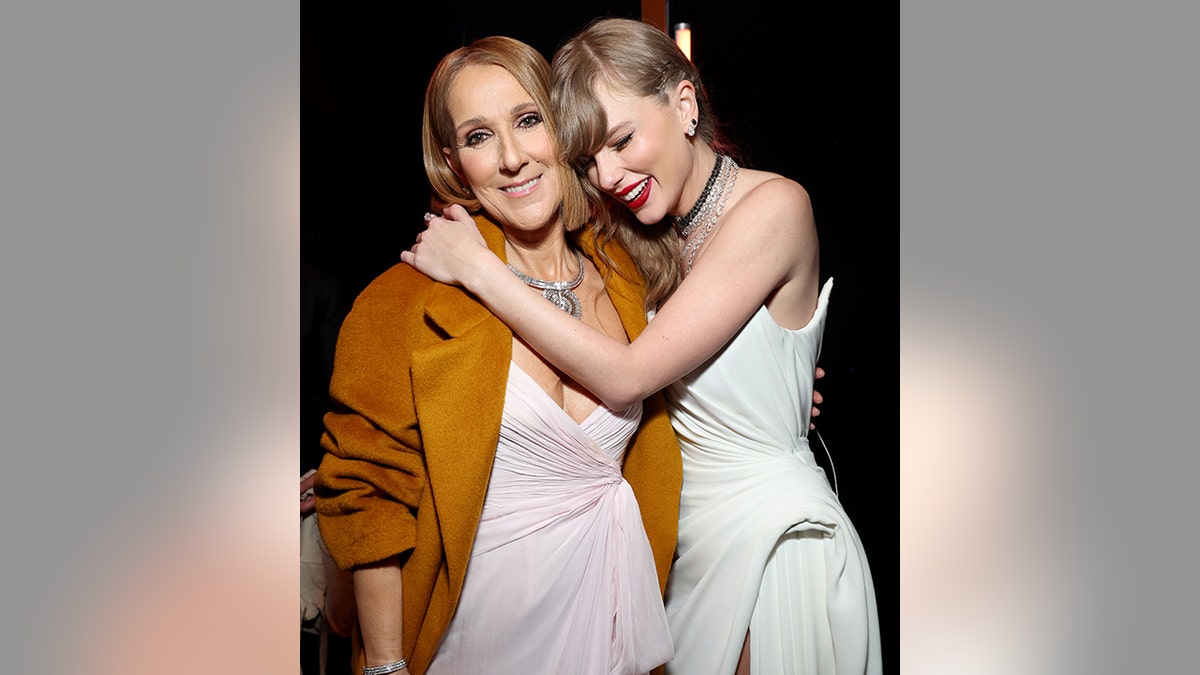 Celine Dion com uma jaqueta laranja queimada sorri ao ser abraçada por Taylor Swift em um longo vestido branco no Grammy