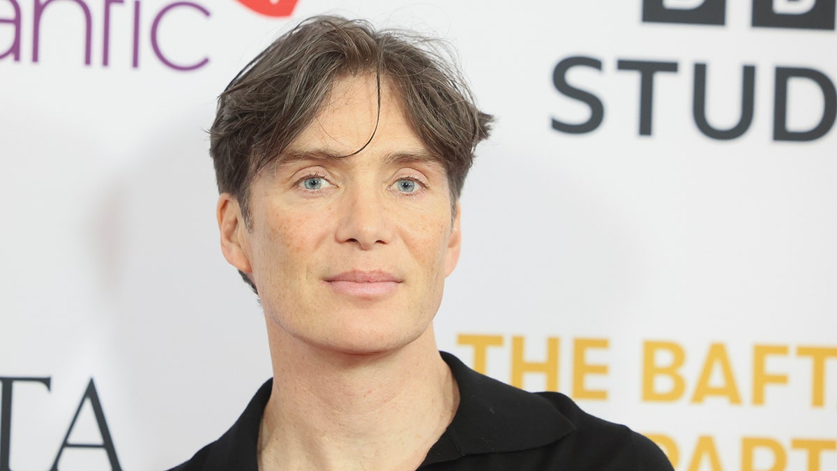 Cillian Murphy soft smiles on the carpet in a black shirt