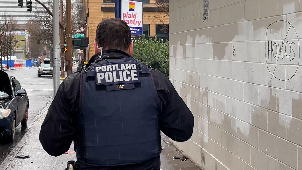 Portland police officer walks by wall with word "Hondos" written on it and a circle and slash sign