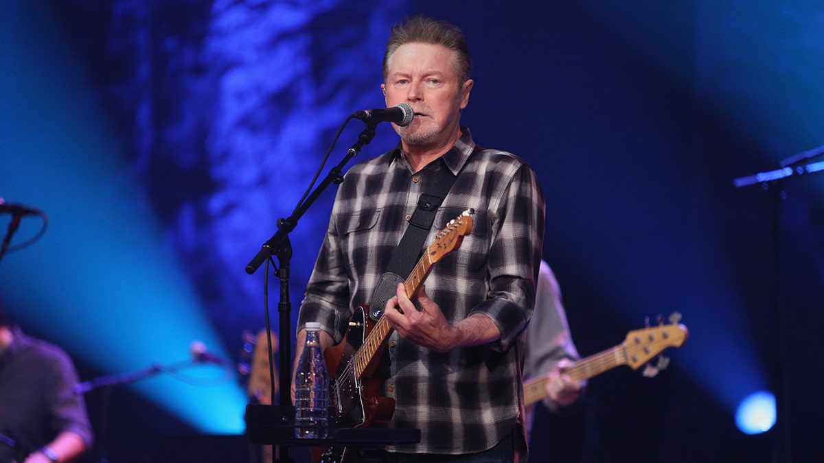 Don Henley strums a guitar wearing plaid shirt
