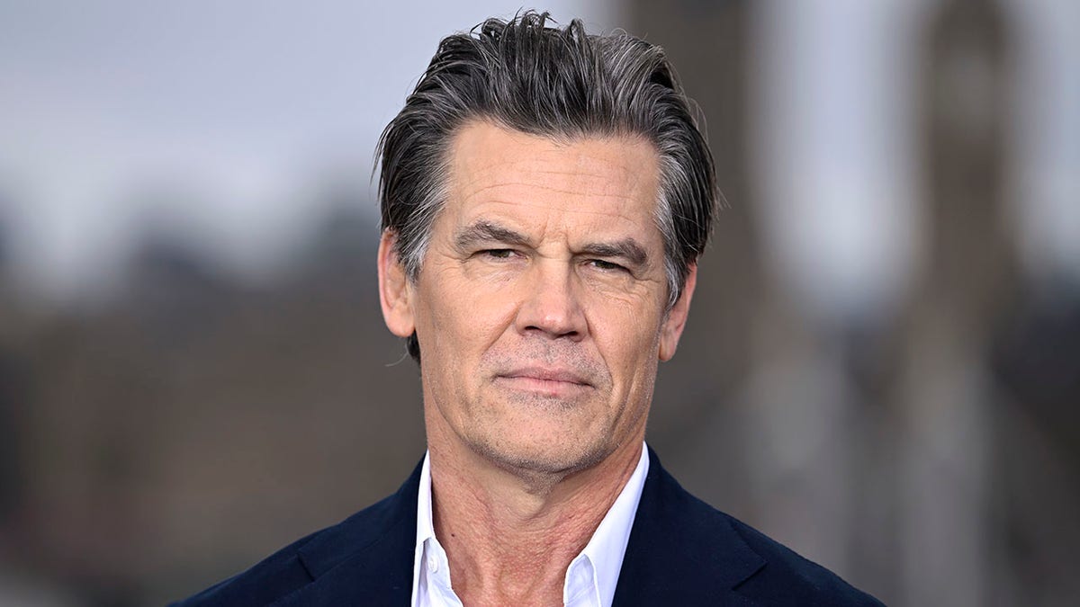 Josh Brolin looks stoic on the carpet in a navy jacket staring directly into the camera