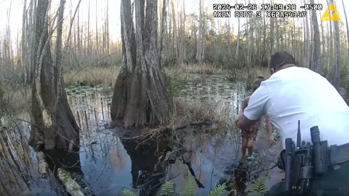 Deputy crouching down to pick up girl in swamp