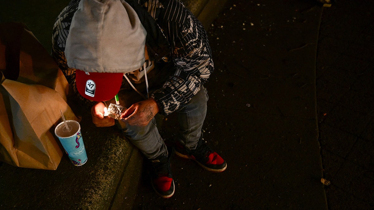 A person smokes a foil of fentanyl at night in downtown Portland