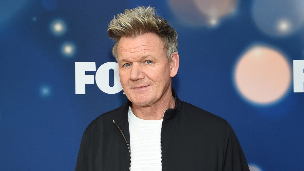 Gordon Ramsay in a white t-shirt and black jacket soft smiles/smirks on the carpet