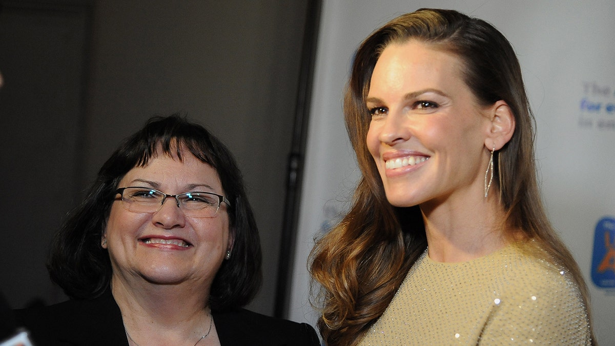 Hilary Swank in a sparkly gown smiles on the carpet next to her mother, Judy