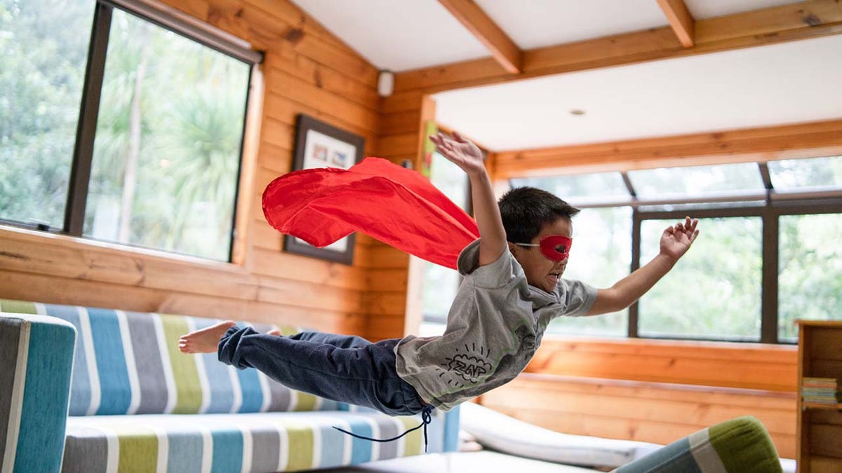 kid dressed as a superhero jumps off the couch