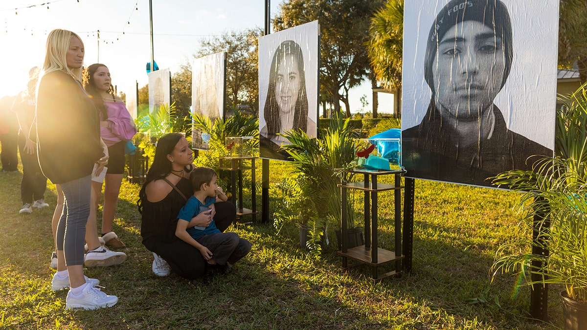 Mariana Rocha holds her son Jackson as she observes a photo of her cousin Joaquin Oliver, right, at a memorial on the fifth anniversary of the Marjory Stoneman Douglas High School mass shooting at Pine Trails Park on Feb. 14, 2023 in Parkland, Florida. On Feb. 14, 2018, 14 students and three staff members were killed during a mass shooting at the school.