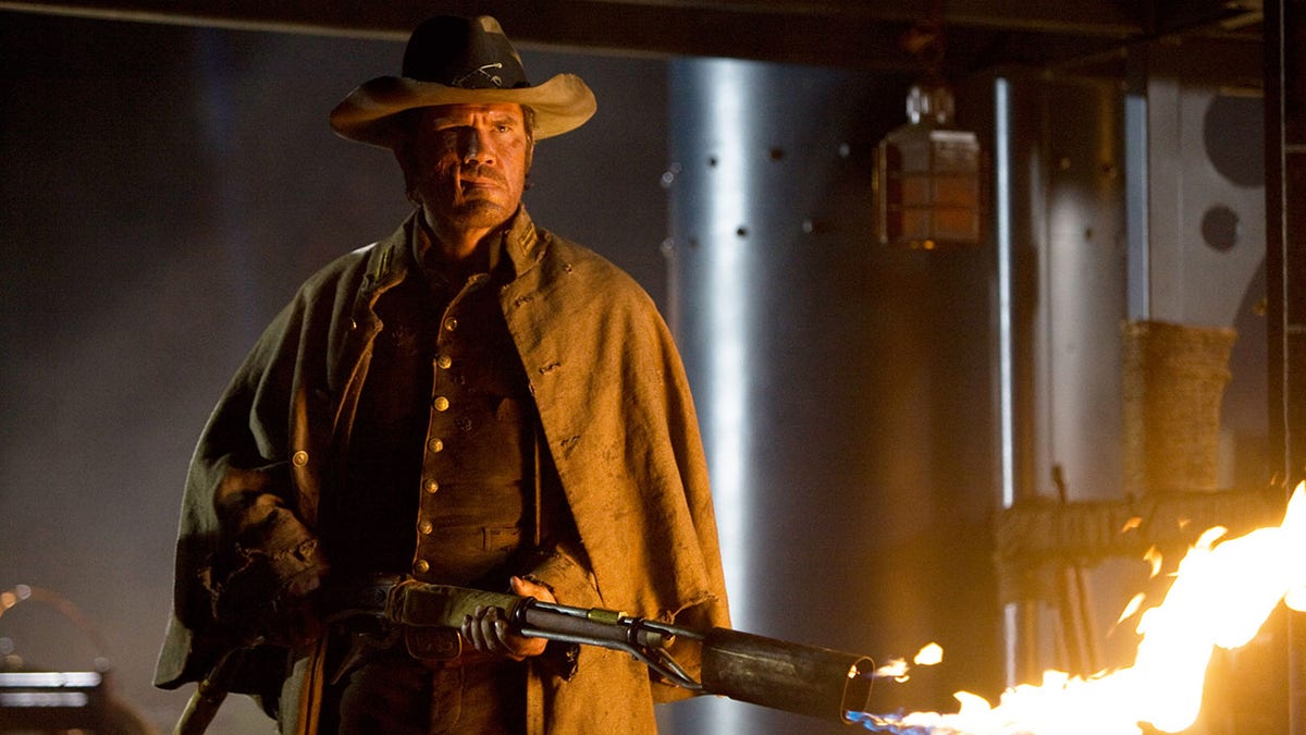 Josh Brolin in "Jonah Hex" with a disfigured face wearing a cowboy hat and holding a weapon shooting fire