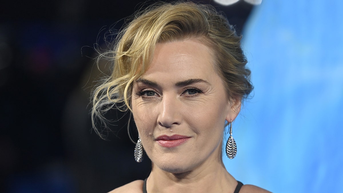 Kate Winslet smirks into the camera on the carpet for "Avatar: The Way of Water"