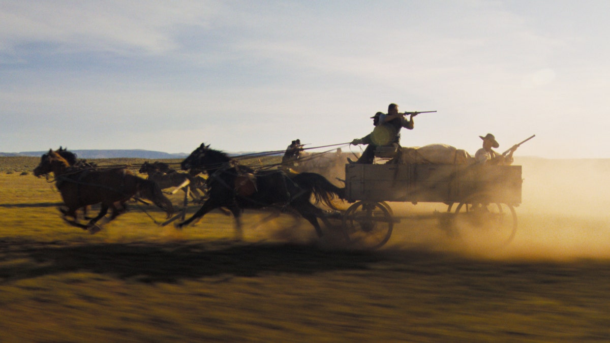 Cowboys shoot guns from the back of a horse-drawn wagon