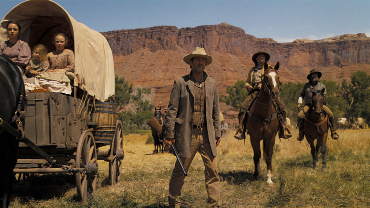 Luke Wilson stands next to a covered wagon in Horizon trailer