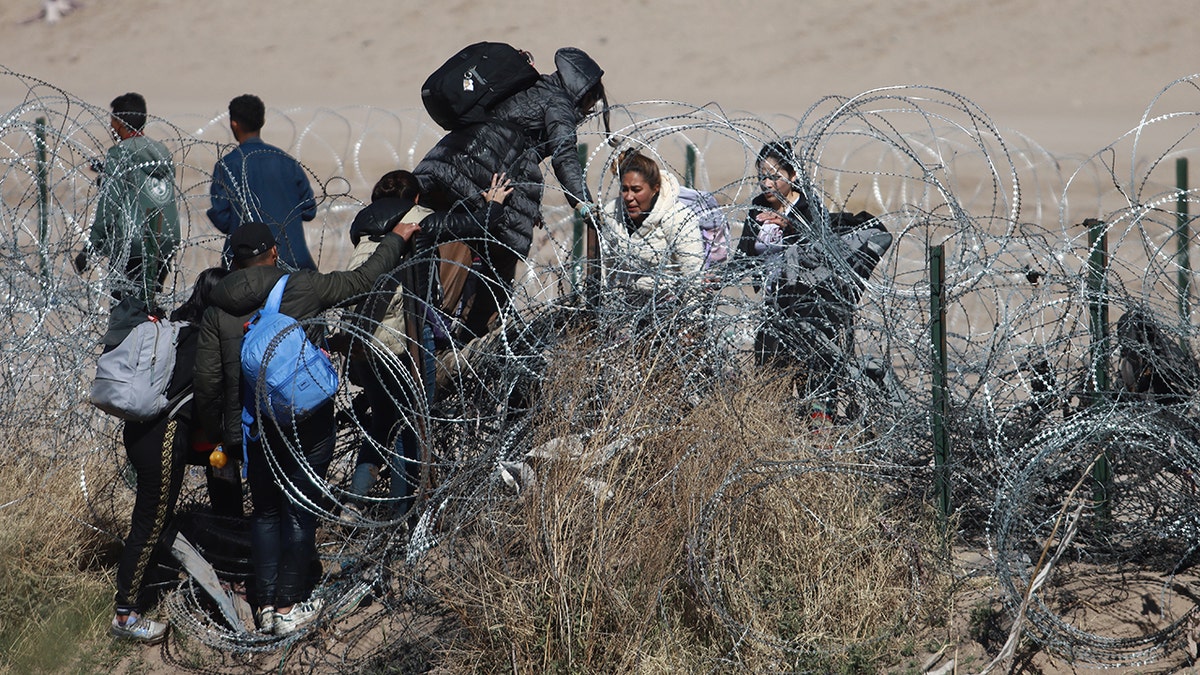 Migrants cross over razor wire at the U.S.-Medico border in Texas