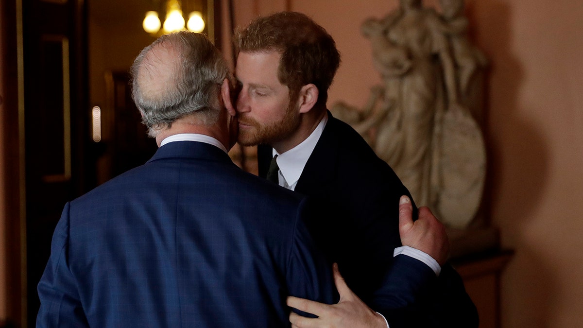 Prince Harry in a black suit kisses King Charles in a navy suit