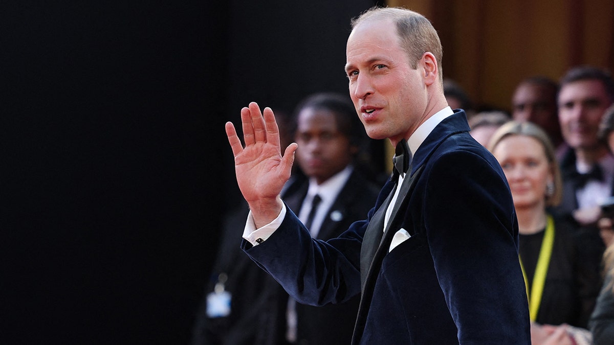 Prince William in a navy velvet tuxedo waves as he attends the BAFTAS