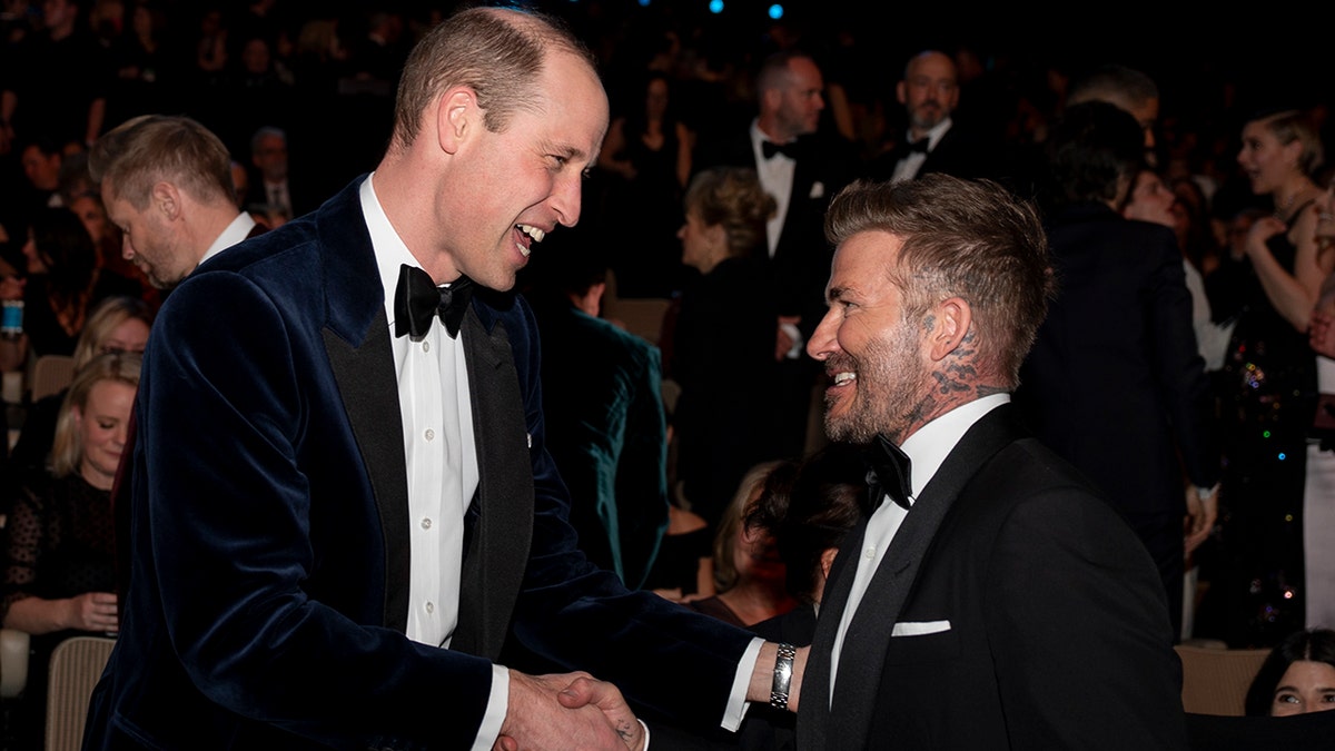 David Beckham shakes hands and smiles down at David Beckham, also wearing a tuxedo