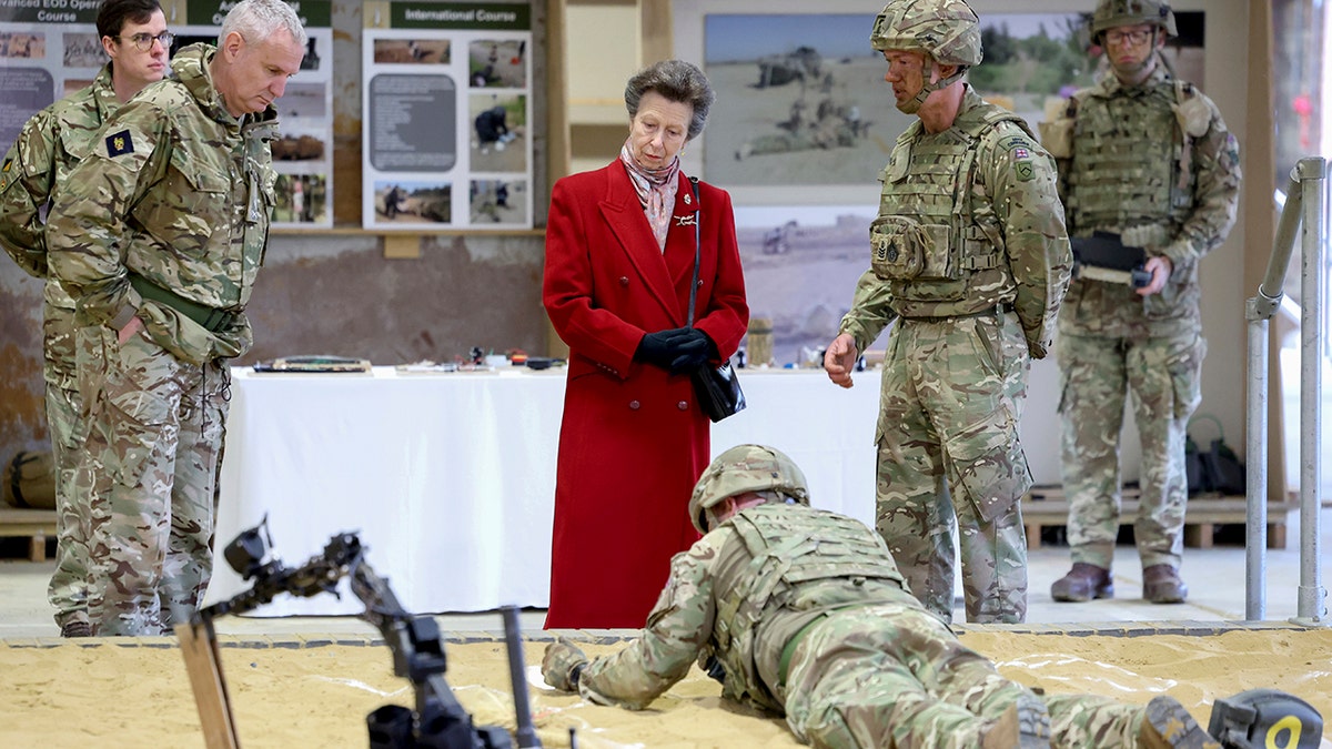 Anne, Princess Royal in a red wool coat attends to royal duties, speaking with military personnel 
