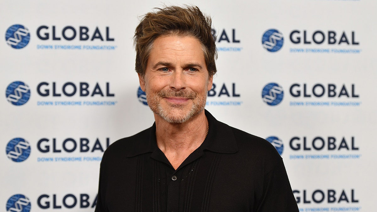 Rob Lowe in a black sweater soft smiles on the carpet and looks slightly to his left
