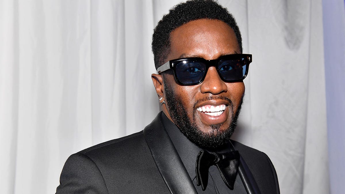 Diddy smiles in a satin-like all black tuxedo and black sunglasses