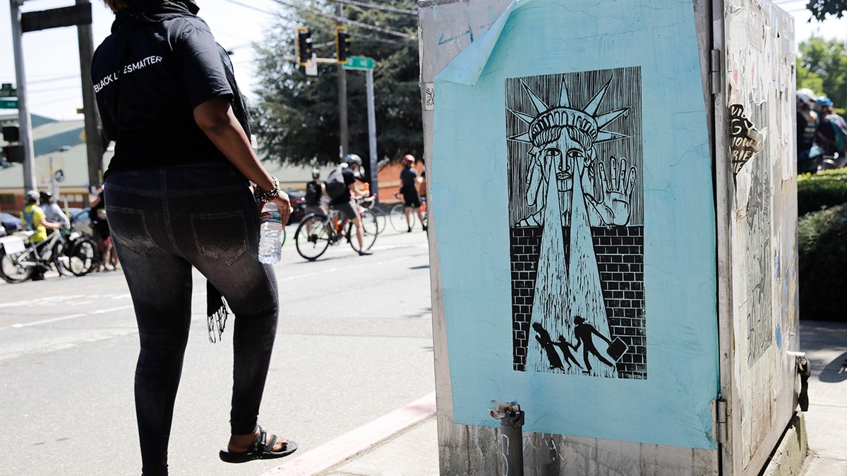 A woman walks by a street poster depicting Lady Liberty preventing an immigrant family from crossing the wall, during a "Defund the Police" march from King County Youth Jail to City Hall in Seattle, Washington on August 5, 2020. 