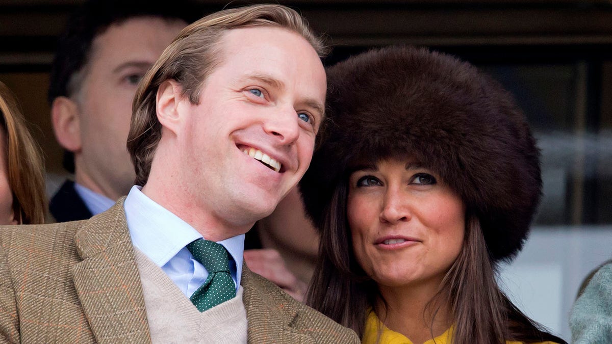 Pippa Middleton in a brown hat looks up as she stands next to Thomas Kingston in a tan jacket