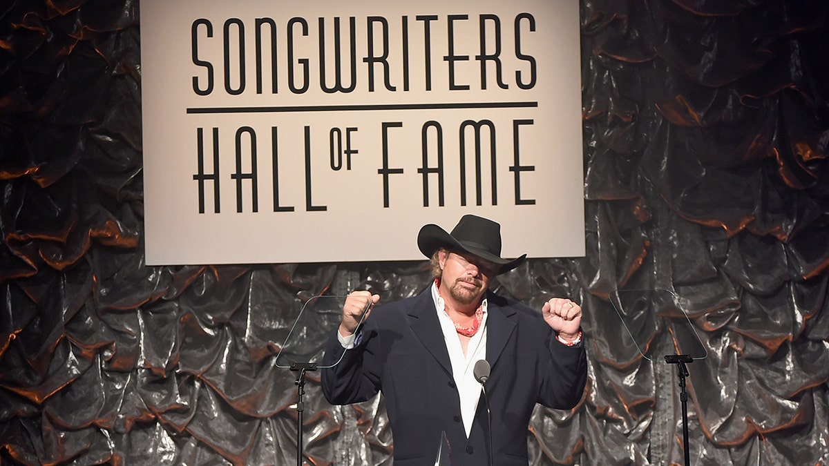 Toby Keith in a black suit and cowboy hat puts his fists in the air at the Songwriters Hall of Fame