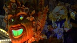 A float with a large head on the front rolls through New Orleans while krewe members aboard throw beads