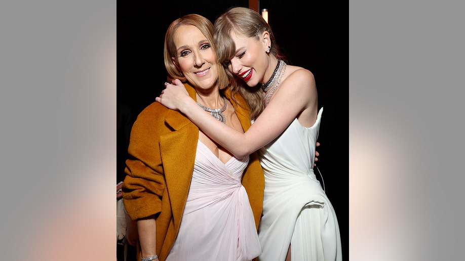 Celine Dion in a burnt orange jacket smiles as she is hugged by Taylor Swift in a long white gown at the Grammys
