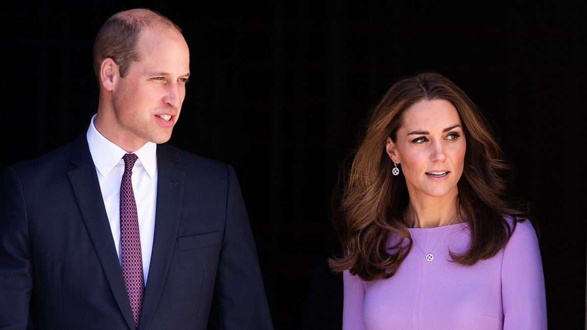 Prince William walking alongside Kate Middleton who is wearing a purple dress