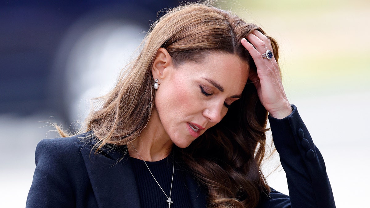 Kate Middleton olha para baixo, passando a mão pelos cabelos, parecendo estressada