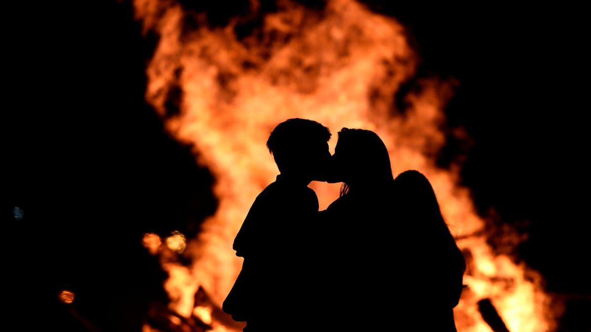 Two people kiss in front of a bonfire