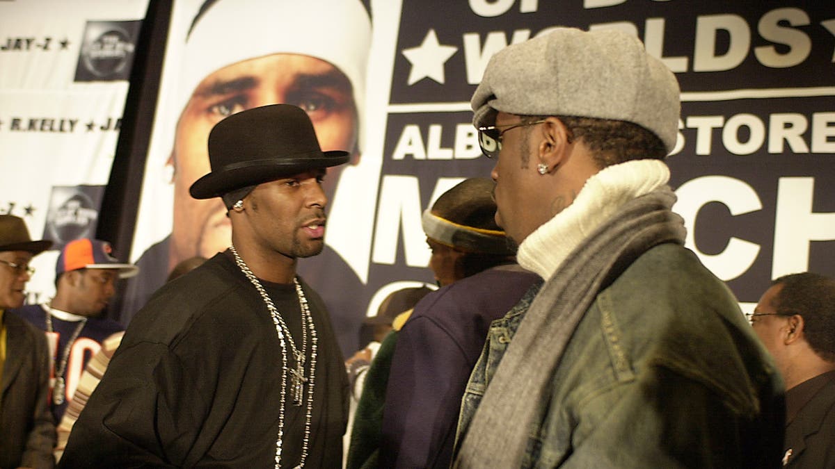 R Kelly in a black t-shirt and bowler hat shakes hands with Diddy, wearing a denim coat, sweater and scarf