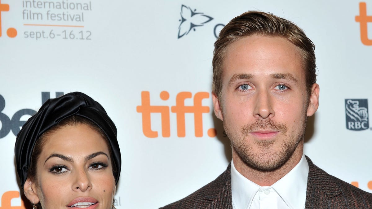 Eva Mendes in a printed dress stands on the carpet next to Ryan Gosling in a brown checkered jacket and white shirt