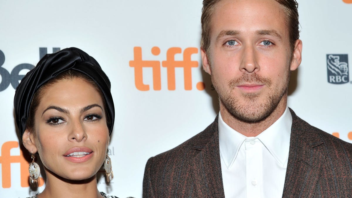 Eva Mendes in a printed dress stands on the carpet next to Ryan Gosling in a brown checkered jacket and white shirt