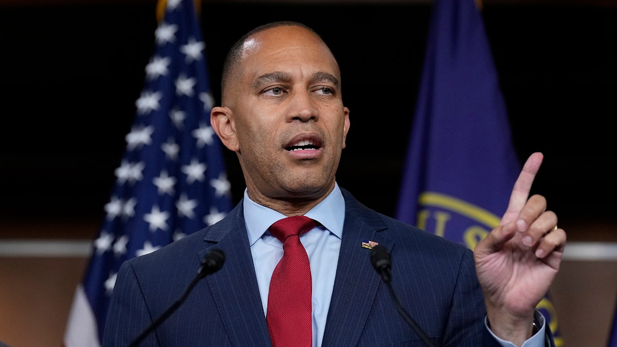 Hakeem Jeffries, left hand in air pointing, US flag behind him