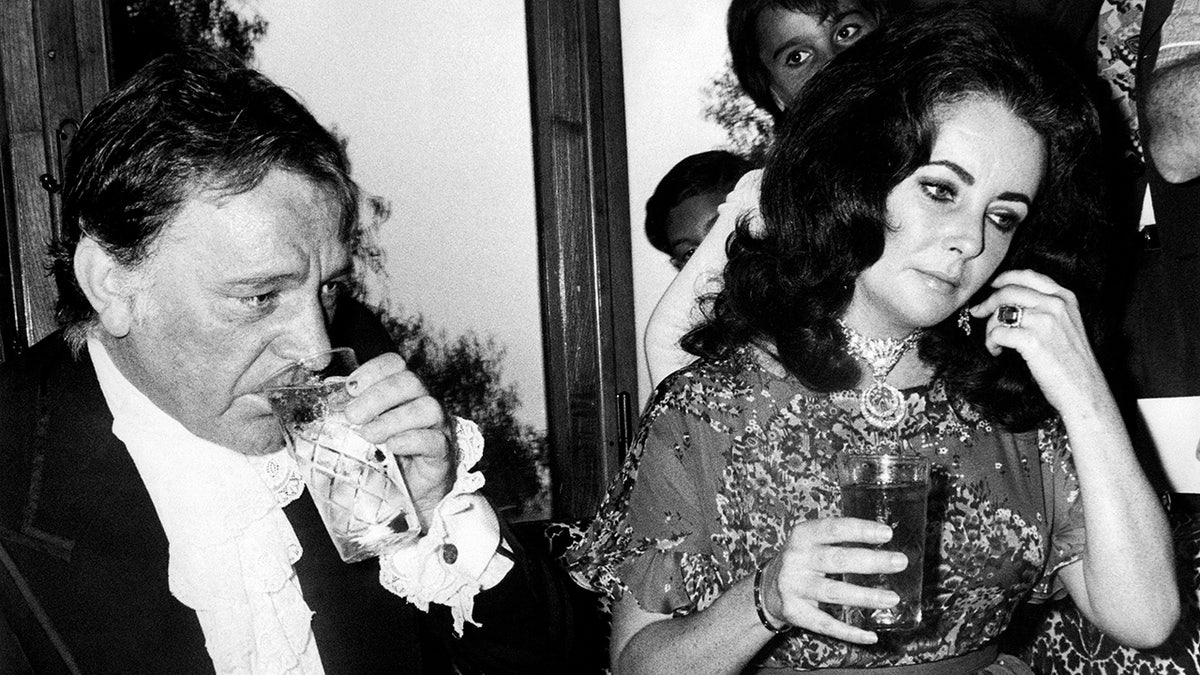 Elizabeth Taylor and Richard Burton holding drinks at the table
