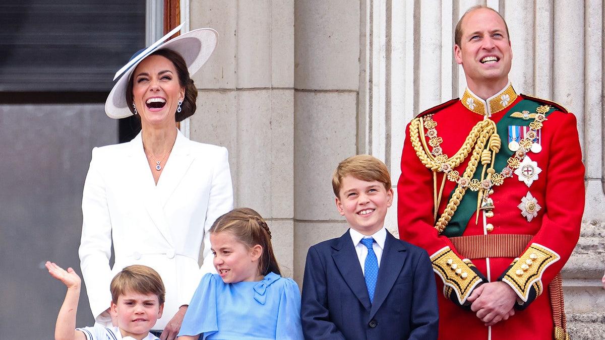 Kate Middleton laughing as she stands next to her husband and their three children