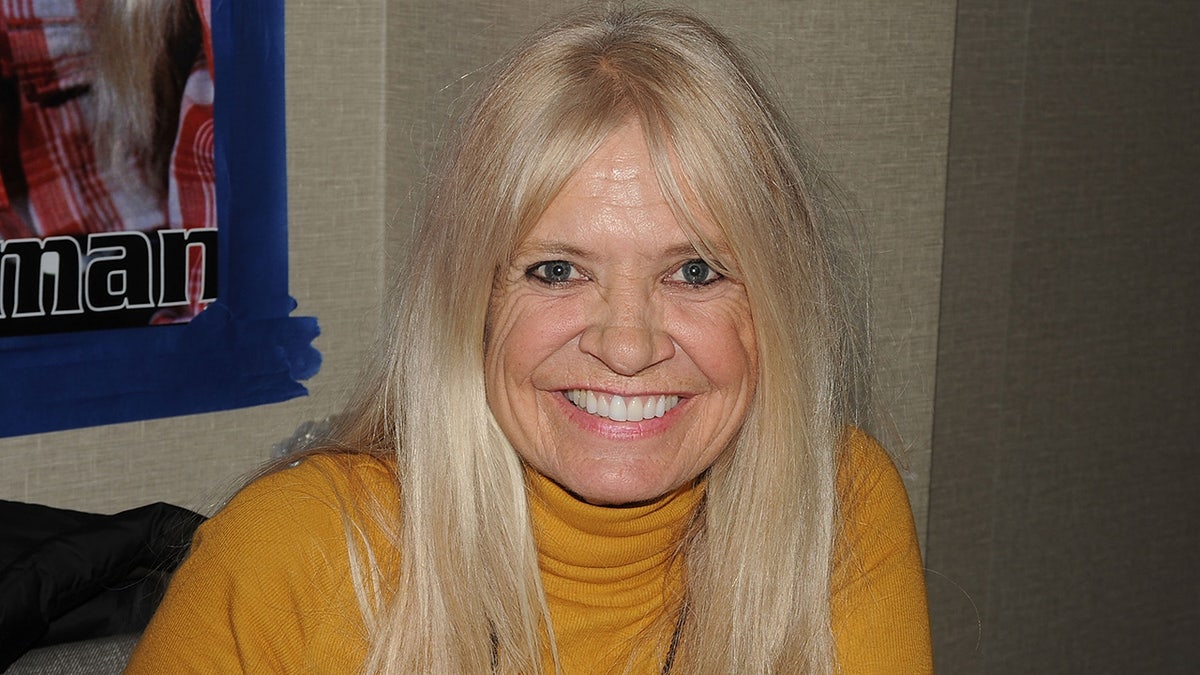 Kathy Coleman sorrindo usando uma gola alta amarela