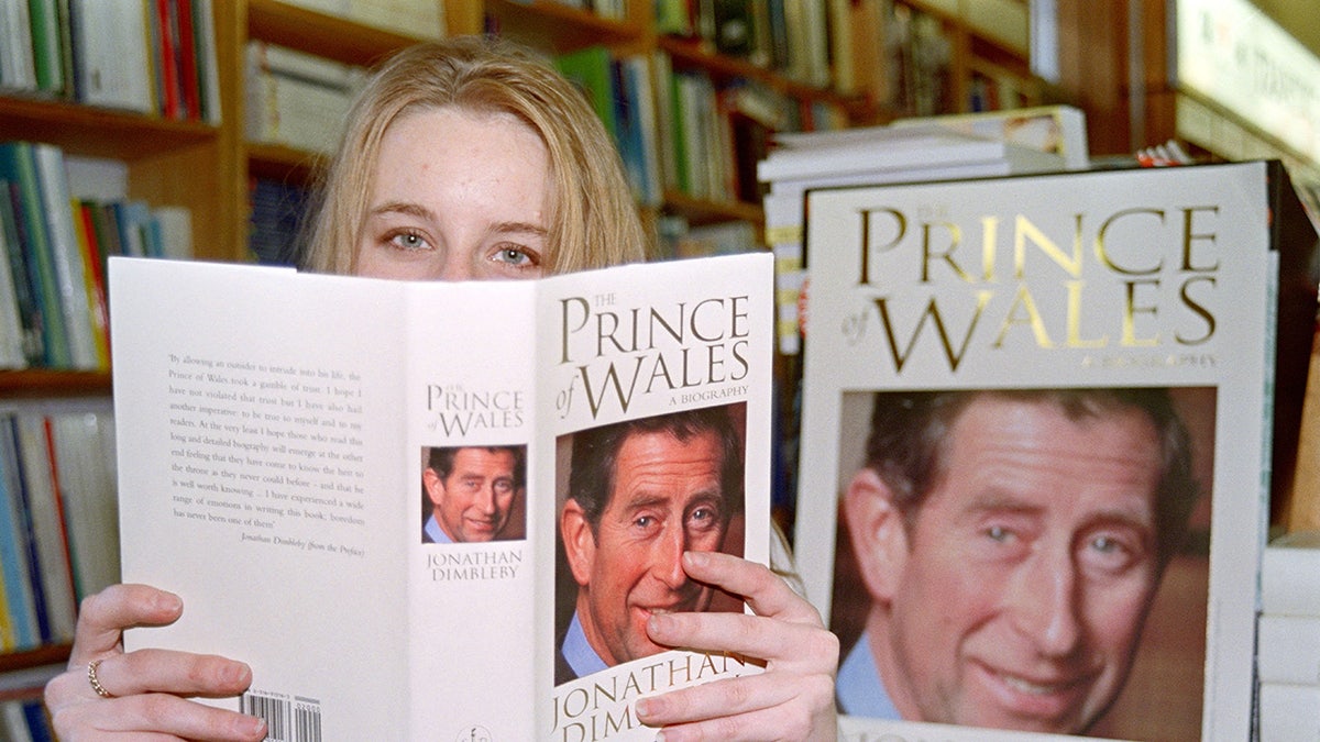 A woman holding a book about King Charles and covering her face with it