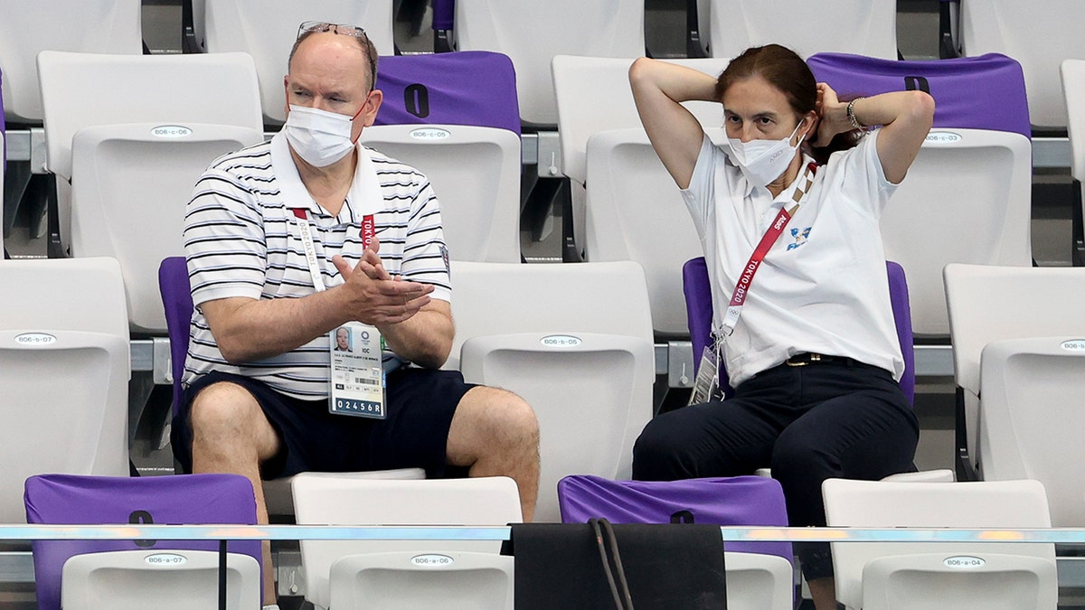 Prince Albert wearing a mask and sitting at the stands with a woman
