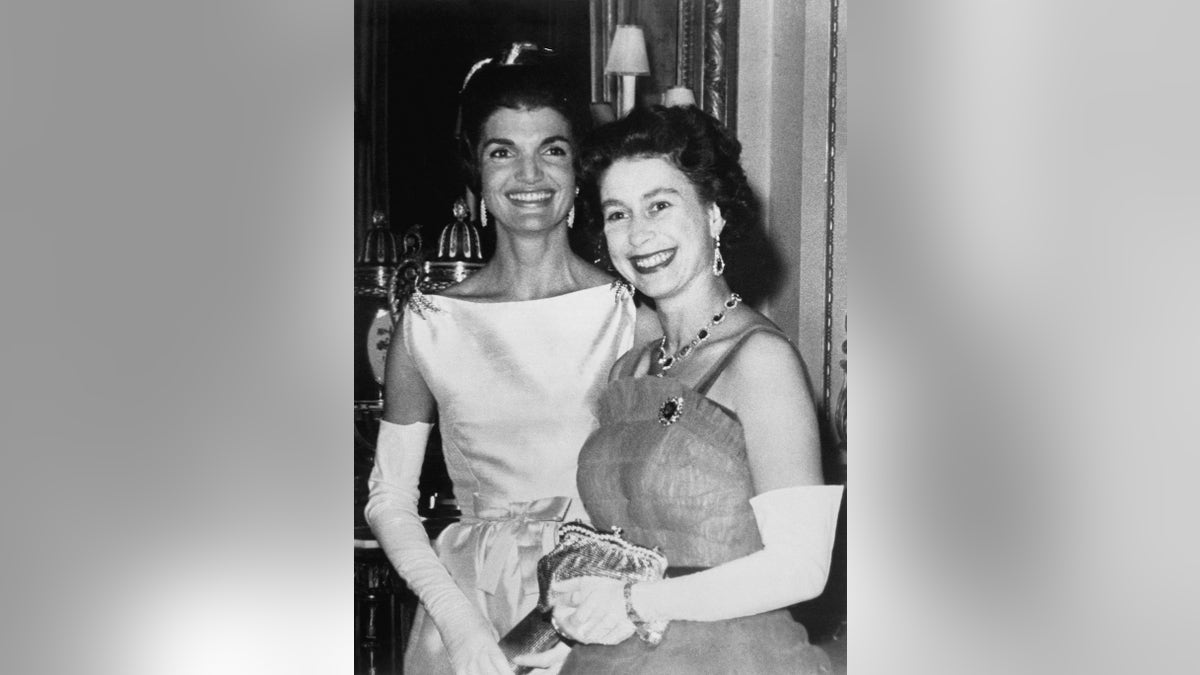 Jackie Kennedy smiling and standing next to Queen Elizabeth II