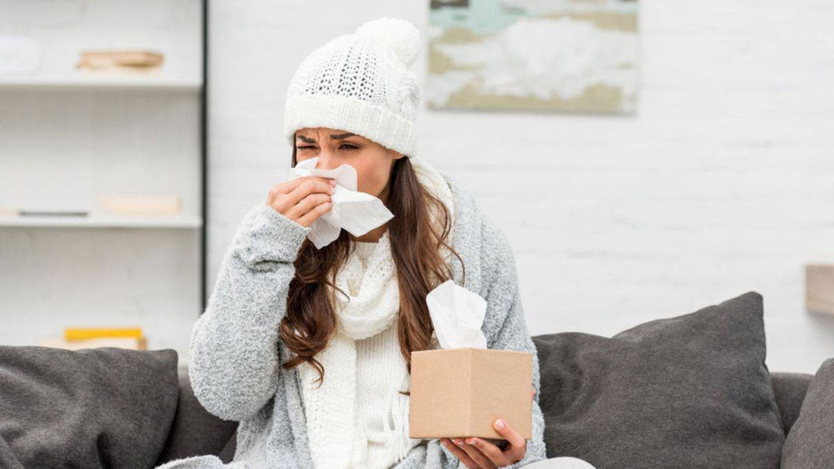 A woman sits on a couch and blows her nose