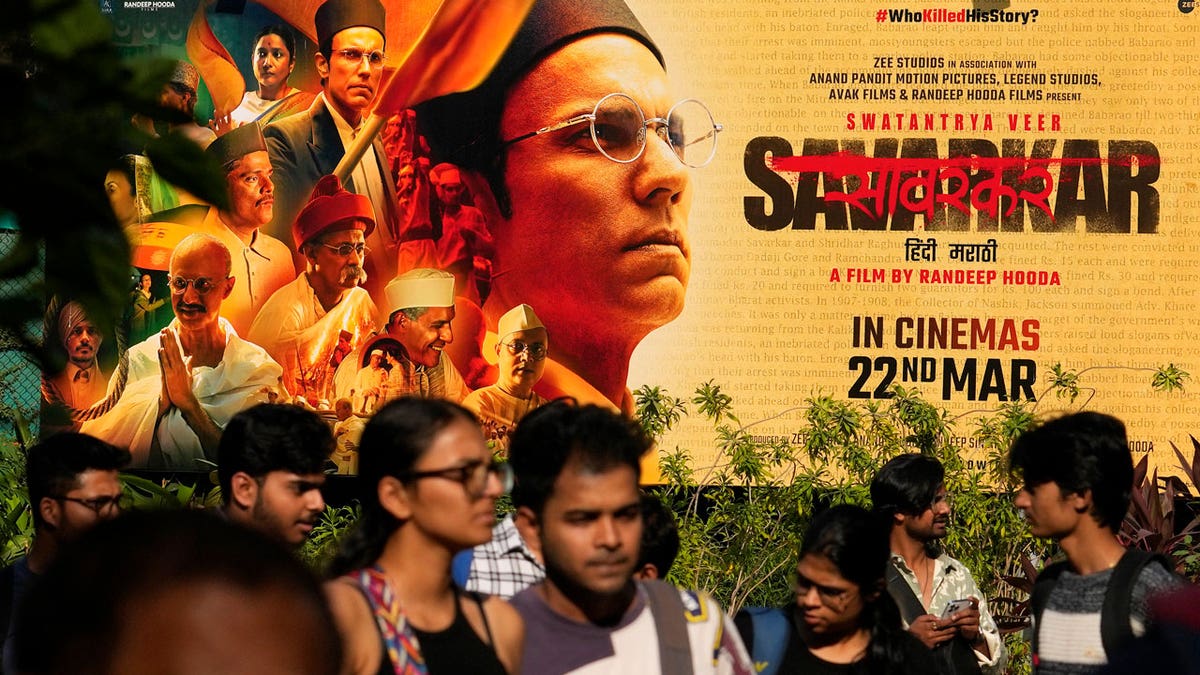 People walk past a large poster of the movie Swatantra Veer Savarkar