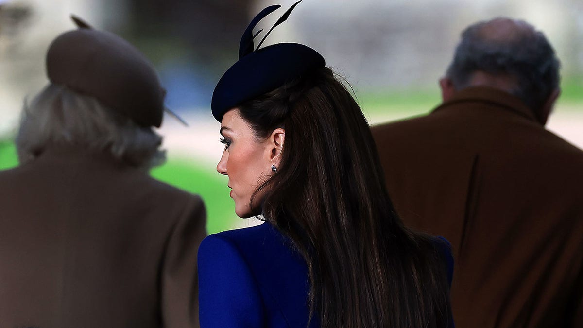 Kate Middleton de costas para a câmera, vestindo um casaco azul e fascinator