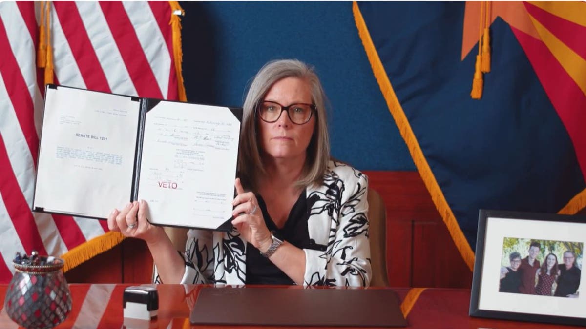 Arizona Governor Katie Hobbs holds up   an migration  measure  she vetoed