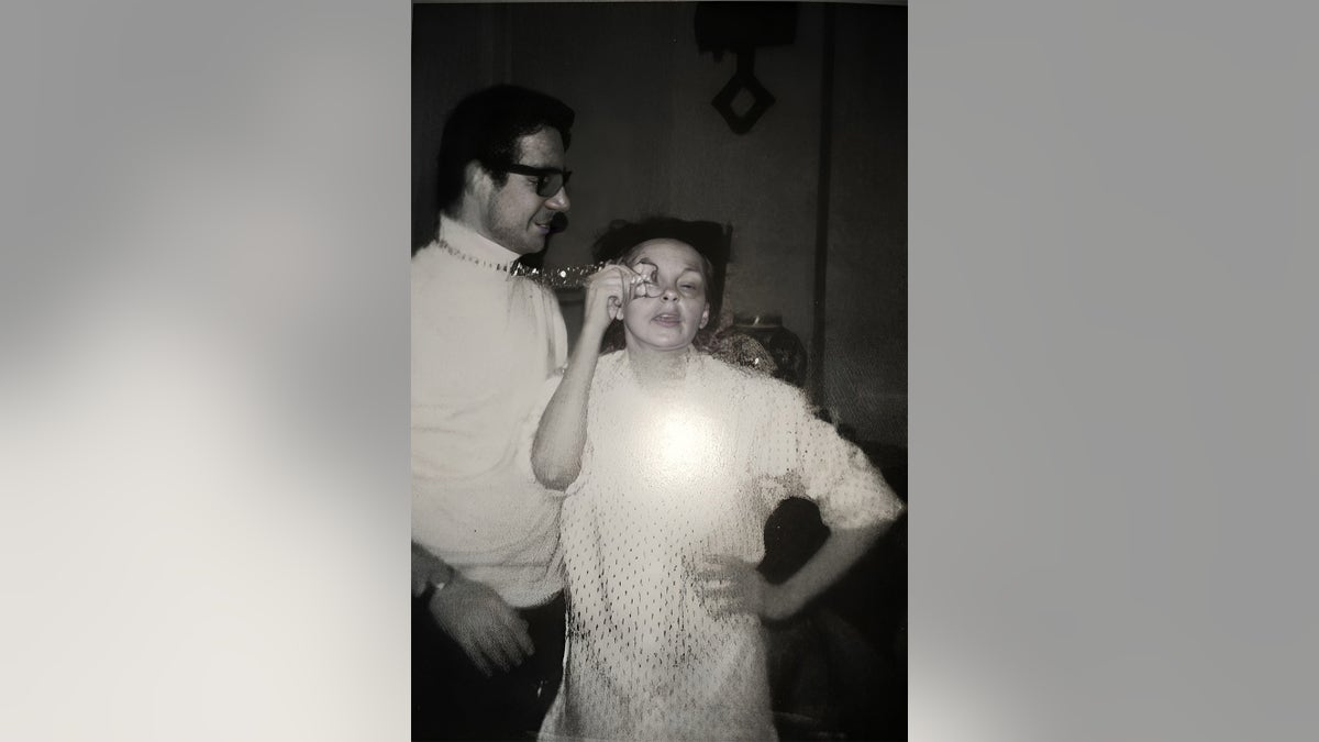 John Meyer standing next to Judy Garland as she applies her eye makeup
