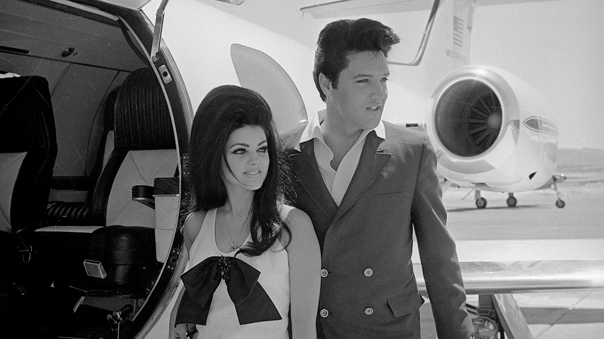 Black and white photo of Priscilla Presley and Elvis Presley standing next to plane