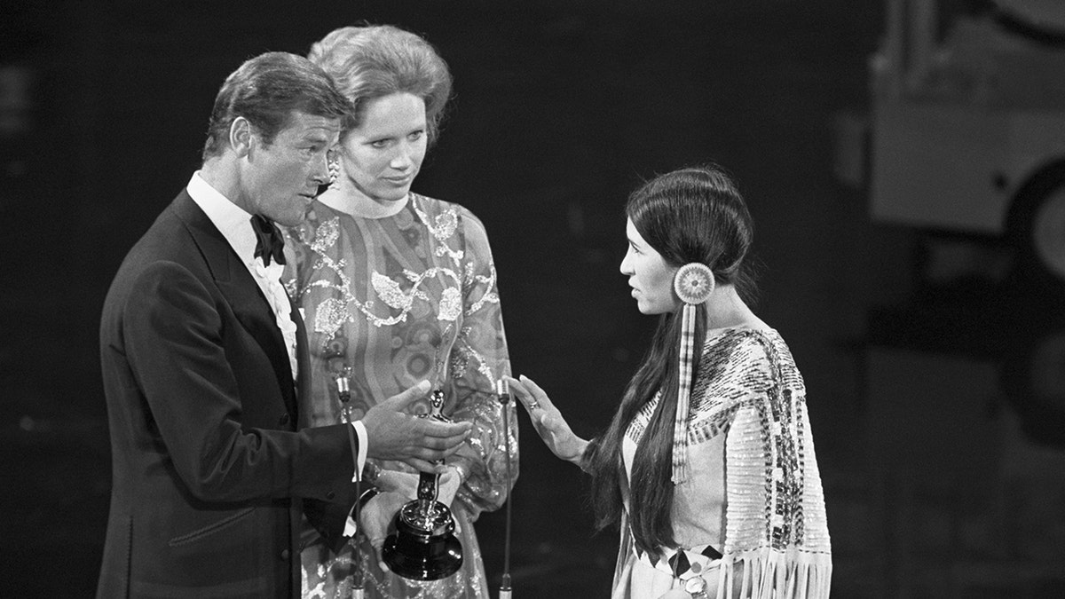 Roger Moore and Liv Ullman on stage with Sacheen Littlefeather at the Oscars