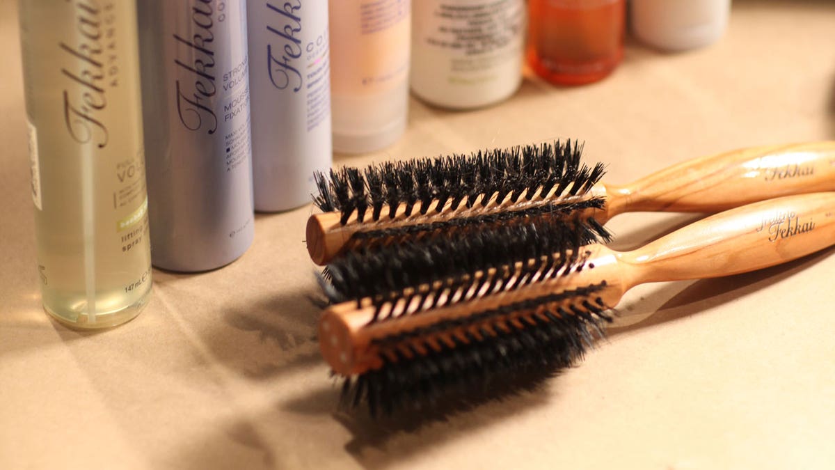 Escovas de cabelo redondas ficam sobre uma mesa em frente a produtos para cabelo