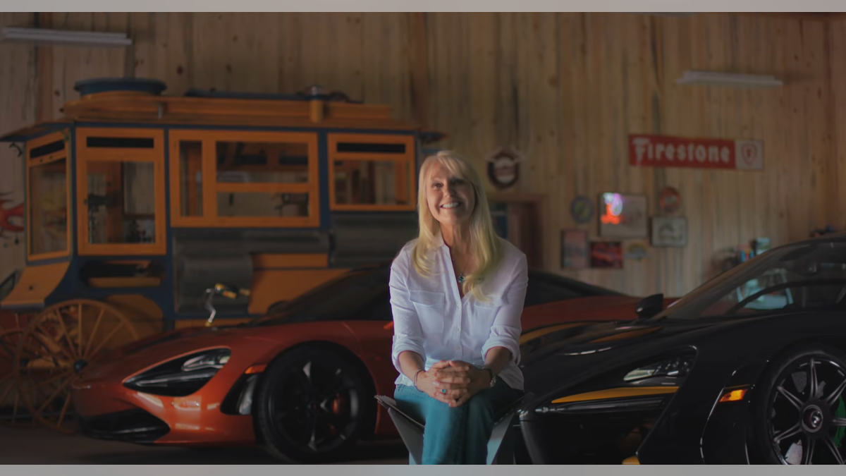Woman sitting in chair with three McLarens parked in the background.